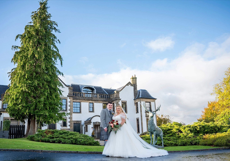 Bride and groom pose outside Gleddoch with deer statue in background